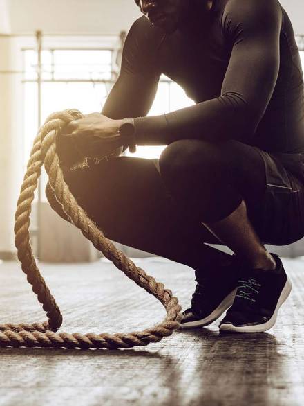 Man sitting on his toes holding a pair of battle ropes for workout. guy at the gym working out with fitness rope.